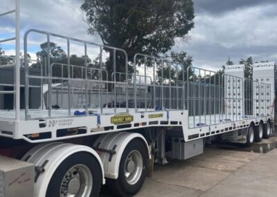 A white Howard Porter drop deck trailer with a silver safety railing around the perimeter and white rear loading ramps. The trailer is parked on a concrete pad under a cloudy sky, showing "Energy Hire" branding and a contact number on the side rail.
