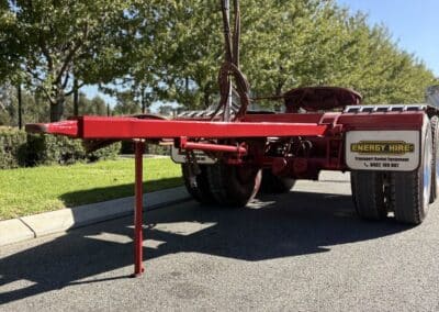 A rear-view of a red Energy Hire converter dolly parked on a paved road with its support leg down.