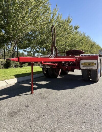 A rear-view of a red Energy Hire converter dolly parked on a paved road with its support leg down.